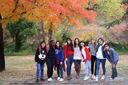 Christian boarding school's, after school club, social media group, stand under, a tree with changing leaves, of orange and red, for the fall season